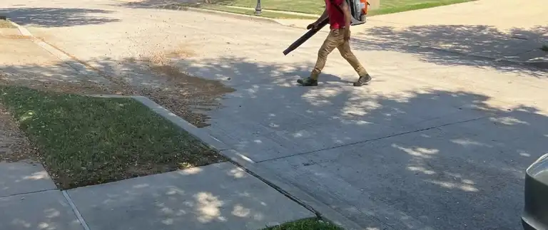 Worker using a leaf blower to clear leaves from a yard