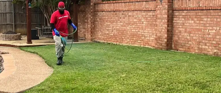 Professional fertilizing a lawn by a brick wall