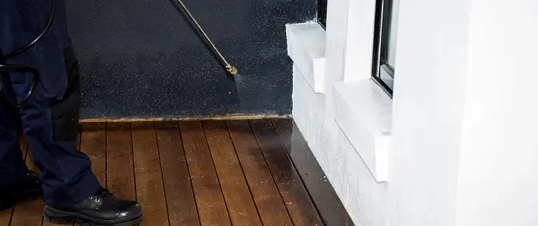 Worker pressure washing a dark exterior wall above a wooden deck in Azle, TX