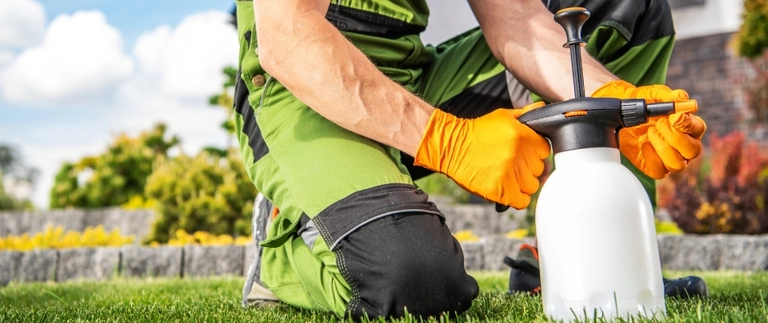 Lawn technician kneeling on grass with handheld sprayer for brown patch treatment