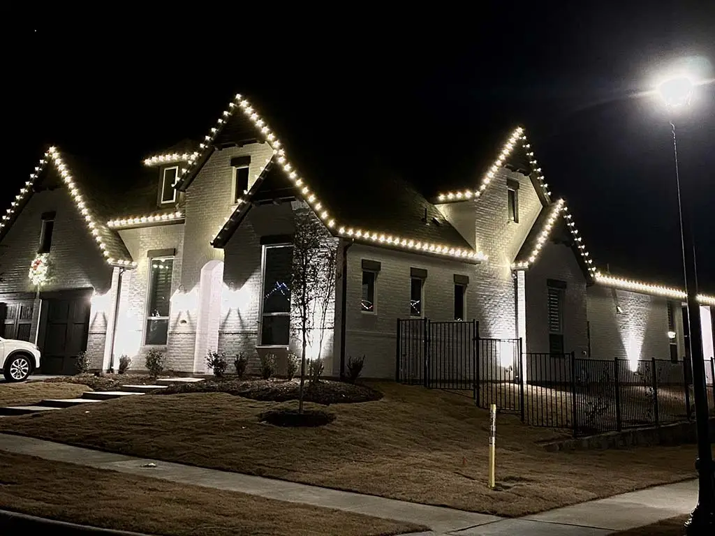 Warm white holiday lights outlining rooflines of a brick home at night in Fort Worth