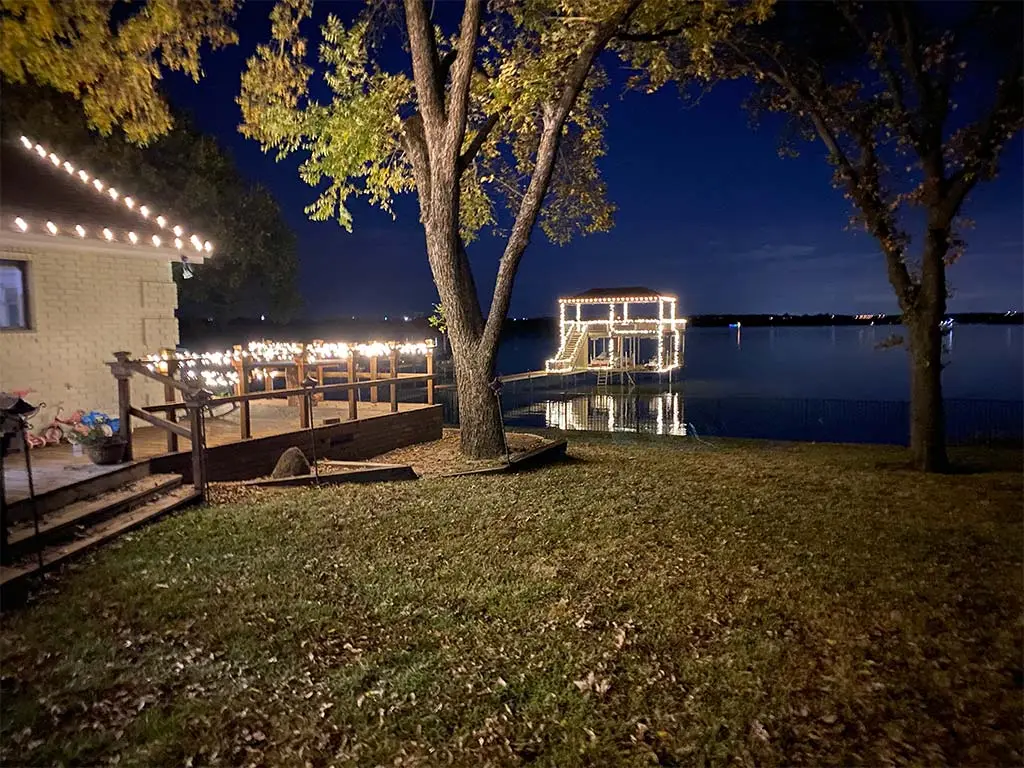 Holiday lights outlining a lakeside boat dock, deck, and home at night