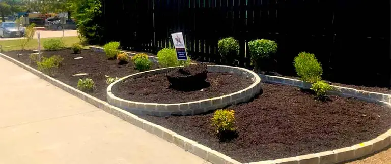 Freshly mulched landscape bed with stone edging and shrubs beside a walkway in Fort Worth