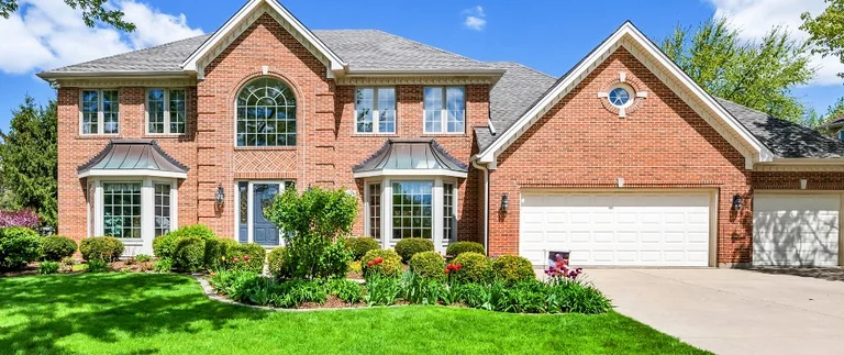 Two-story brick home in Pelican Bay with manicured green lawn and flower beds