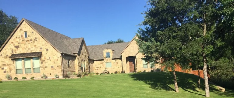 Freshly mowed green lawn in front of a stone home in Pelican Bay, TX