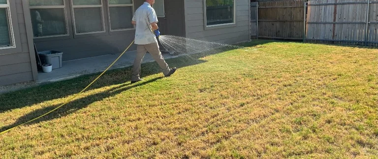 Lawn care technician spraying large patch fungicide treatment on a Fort Worth backyard lawn