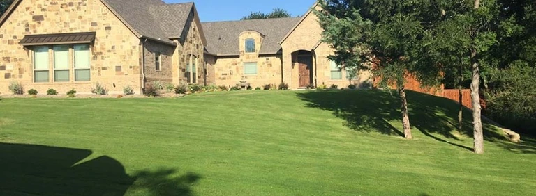 Large stone home with manicured green lawn and mature trees
