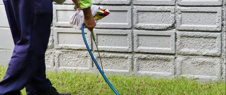 Pest control technician spraying perimeter treatment along concrete block foundation wall