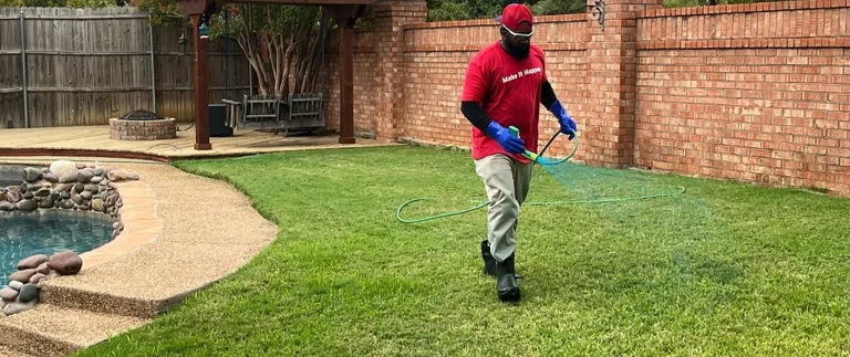 Lawn technician spraying fall fertilizer treatment on backyard grass in Keller, TX