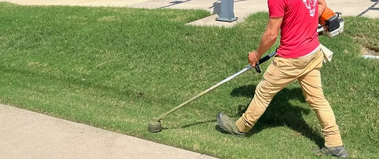 Lawn care technician string trimming grass edge along sidewalk in Haltom City, TX