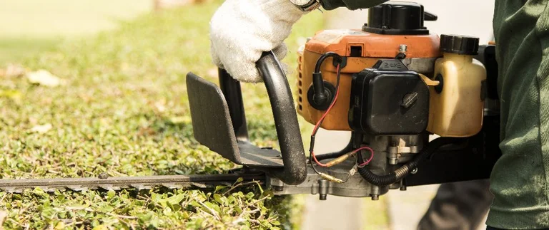 Gloved worker trimming shrubs with gas hedge trimmer during lawn maintenance in Fort Worth