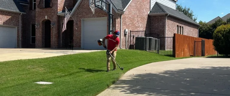 Lawn care technician string trimming grass edge along a Richland Hills home driveway